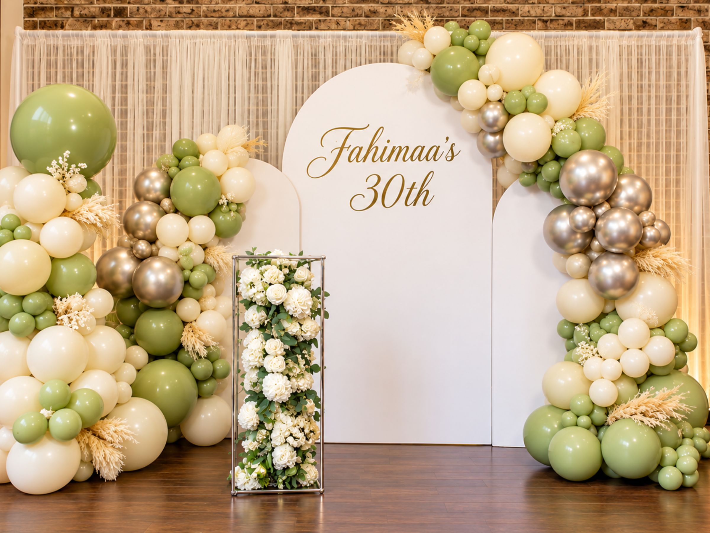 Green, white and gold birthday balloon display with flowers and a backdrop.