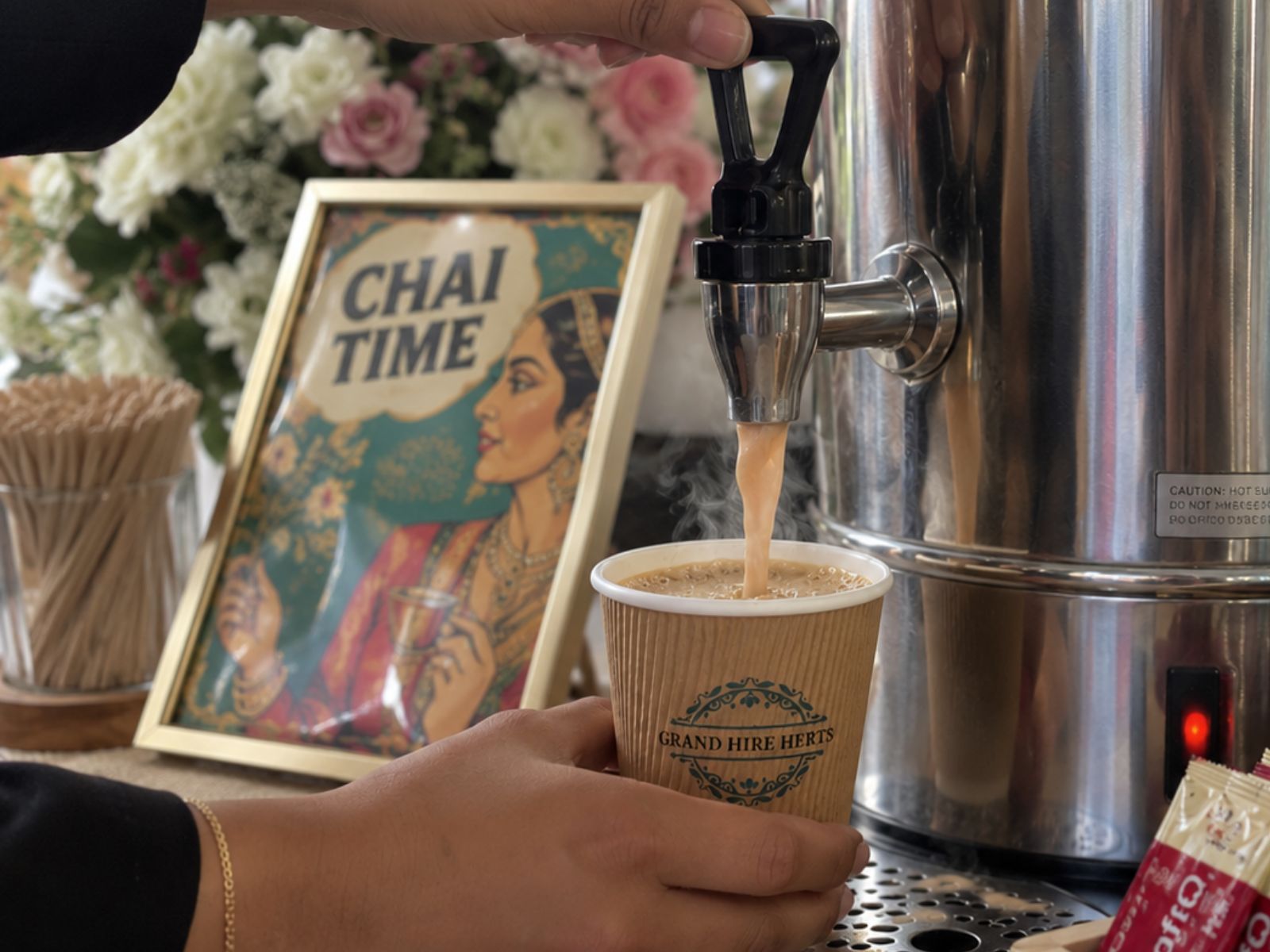 Karak chai being poured into a paper cup beside a decorative sign.